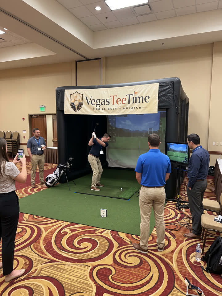 Coworkers watching a teammate swing at the Vegas Tee Time mobile golf simulator during a team-building event in a hotel conference room
