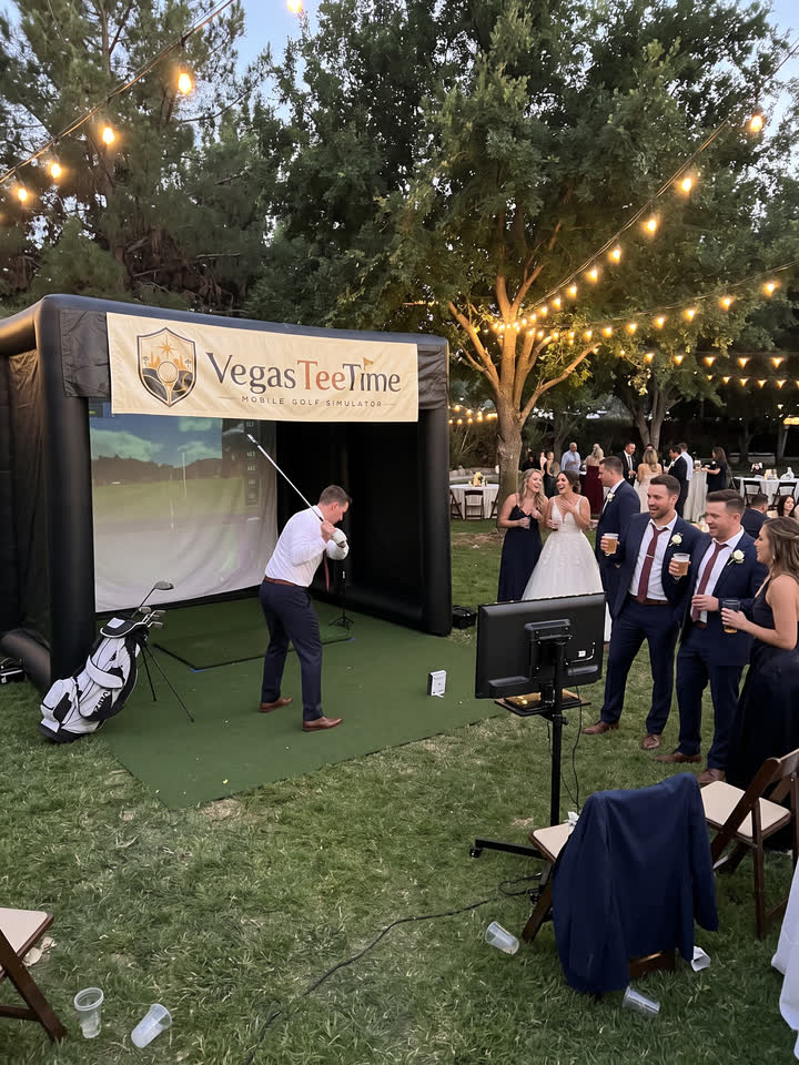 Groom swinging at the Vegas Tee Time mobile golf simulator as the bride and guests watch at an evening wedding reception